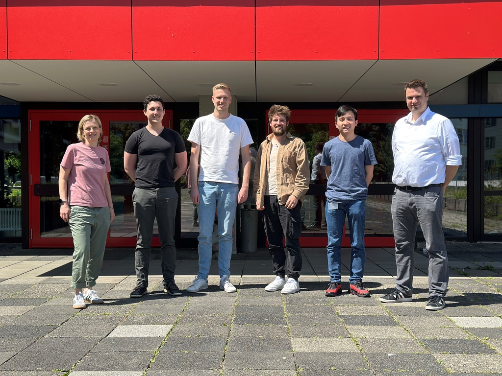 Eine Gruppe von sechs Personen vor einem Gebäude mit roter Fassade.